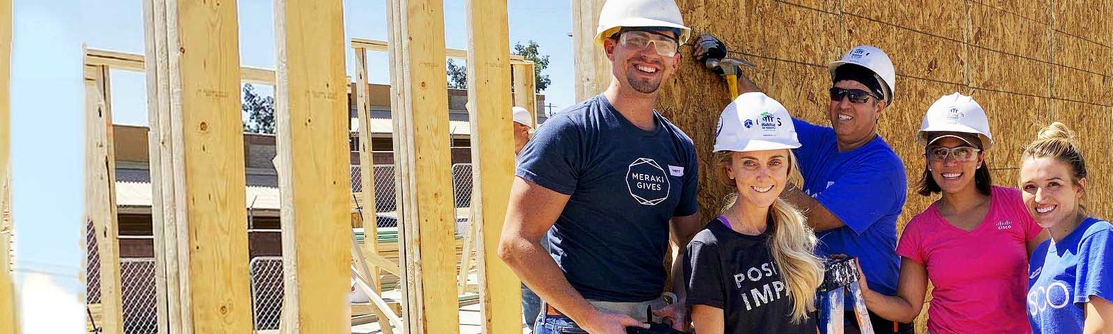 Five employees smiling wearing hard hats as they build a house for a team volunteer event