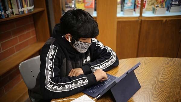 Boy with mask on securely doing schoolwork on a tablet computer