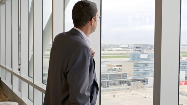 Man in suit looking out large window at Aéroports de Montréal 
